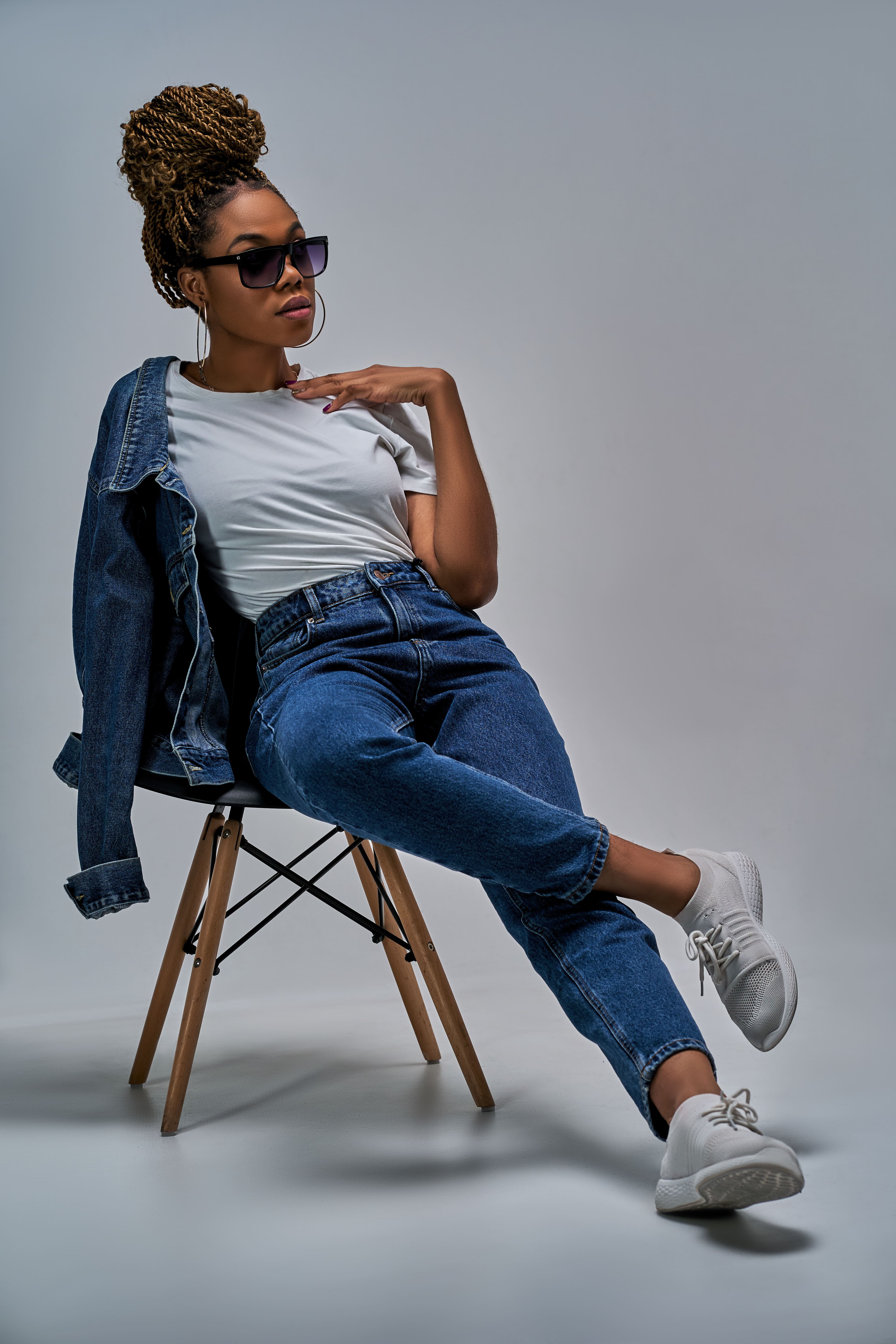 Mulher sentada em uma cadeira usando calças jeans com um fundo cinza